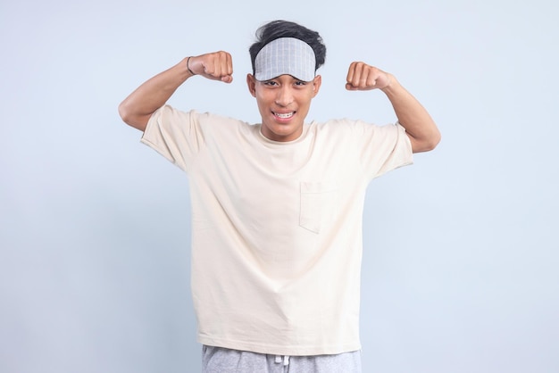 Aufgeregter junger Mann trägt eine Augenmaske und zeigt starke Hände, Bicepsmuskeln über einem hellblauen Hintergrund isoliert