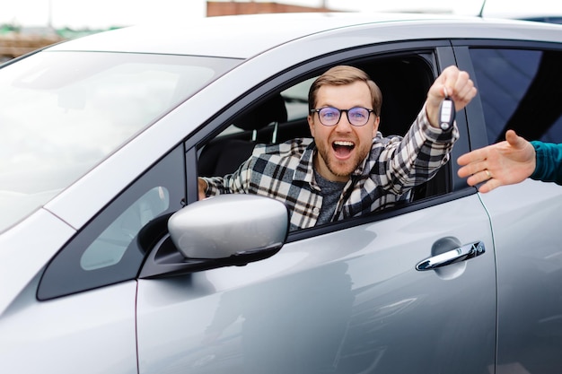 Aufgeregter junger Mann zeigt einen Autoschlüssel, der in seinem neuen Fahrzeug sitzt