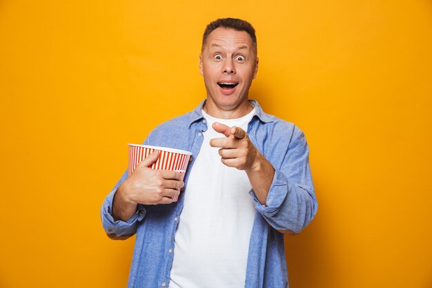 Aufgeregter Mann lokalisiert über gelbe Wand, die Popcorn essen Film schauen.