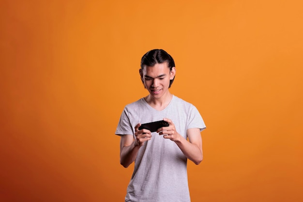 Aufgeregter Teenager, der Videospiele am Telefon spielt, junger asiatischer Mann, der Spaß hat und Online-Videospiele für Mobilgeräte genießt. Internet-Freizeitaktivität, fröhlicher Spieler mit Smartphone-Unterhaltungsanwendung