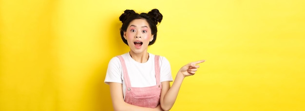 Aufgeregtes asiatisches Teenager-Mädchen, das mit dem Finger nach links auf das Logo zeigt und glücklich aussieht, wenn es Werbung zeigt