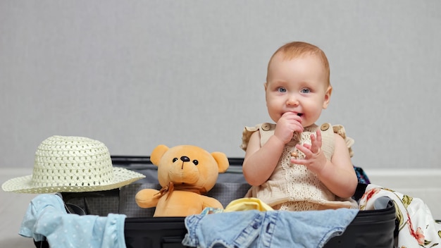 Aufgeregtes Babymädchen beißt Finger und genießt Reise im Koffer