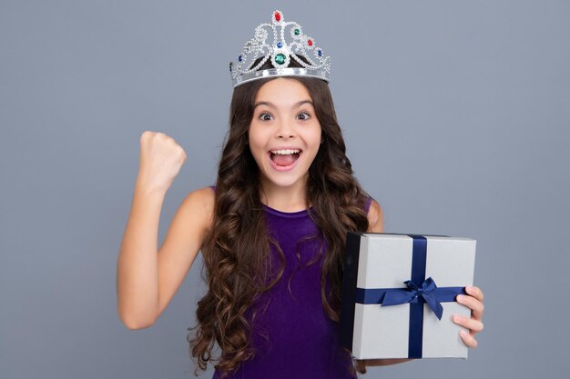 Aufgeregtes Gesicht fröhliche Emotionen von Teenager-Mädchen Kind Teenager-Mädchen 1214 Jahre alt mit Geschenk auf grau