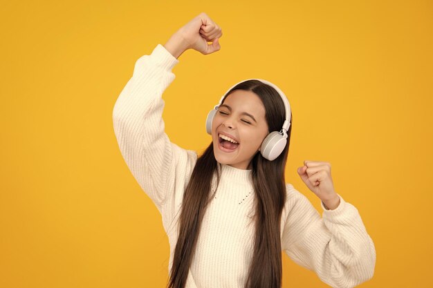 Aufgeregtes Gesicht Teen Girl in Kopfhörern Musik hören Wireless-Headset-Gerät Zubehör Kind genießt die Musik in Kopfhörern auf gelbem Hintergrund Erstaunt Ausdruck fröhlich und froh