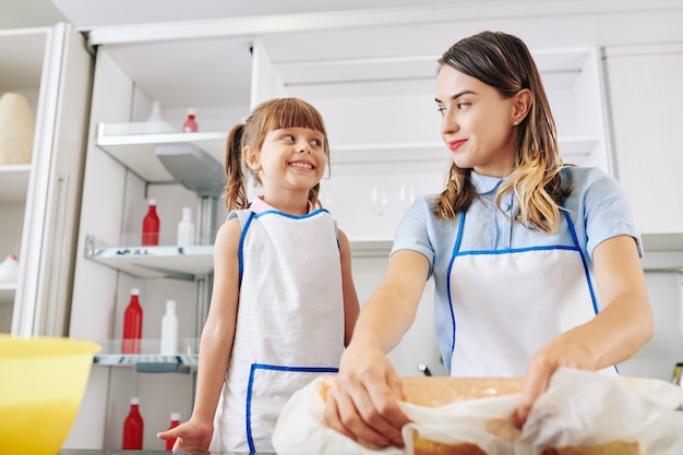 Aufgeregtes kleines Mädchen, das ihre Mutter betrachtet, die Kuchen mit Schlagsahne und Mandarine innen rollt