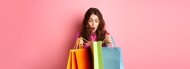 Aufgeregtes Mädchen öffnet Einkaufstüten und schnappt nach Luft, als sie Geschenke für sie mit fröhlichem Gesicht auscheckt