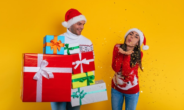 Aufgeregtes modernes Paar verliebt in viele bunte Geschenkboxen in den Händen, während sie Weihnachten und Neujahr feiern und Spaß haben