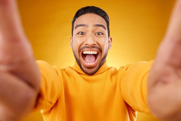 Aufgeregtes Porträt und Selfie eines glücklichen Mannes im Studio, isoliert auf gelbem Hintergrund, Gesichtslächeln und einer asiatischen Person, die ein Profilfoto für lustige Erinnerungen, Lachen und Fotografieren in sozialen Medien macht