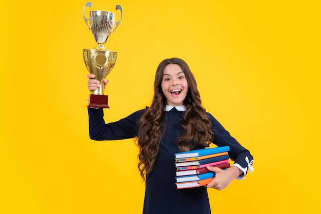 Aufgeregtes Schulmädchen in Schuluniform, das den Sieg mit der Trophäe feiert Jugendlich mit Gewinnerpreis