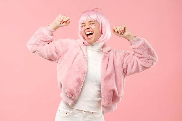 Aufgeregtes Teenagermädchen, das zu Musikklängen tanzt und jubelt, mit flauschigem Pelzmantel und farbigen Haaren auf einer Party