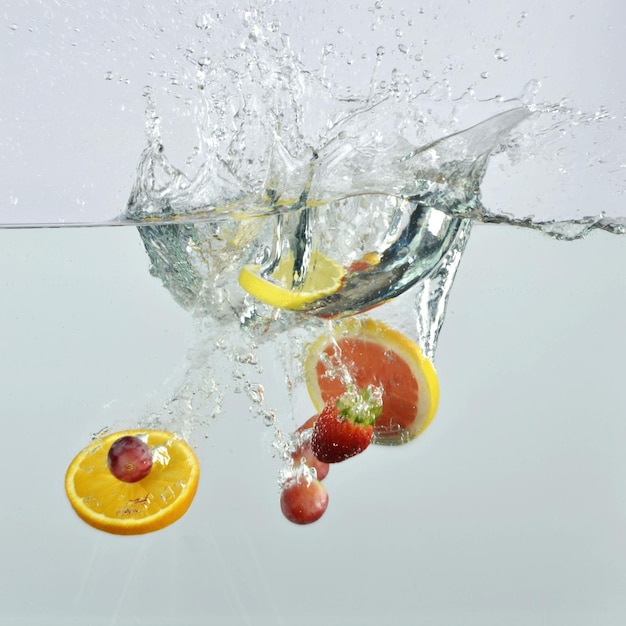 Foto aufgeschnittene orangen mit beeren, die auf wasser gegen weißen hintergrund spritzen