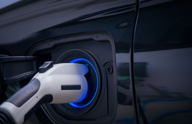 Aufladen der modernen Elektroautobatterie auf der Straße, die die Zukunft des Automobils sind, Abschluss oben der Stromversorgung verstopft in ein Elektroauto, das für Hybrid aufgeladen wird. Neue Ära des Fahrzeugtreibstoffs.