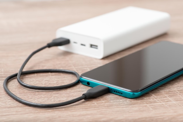 Aufladen des modernen Smartphones von der weißen Powerbank Power Bank und Mobiltelefon während des Ladevorgangs auf dem Tisch