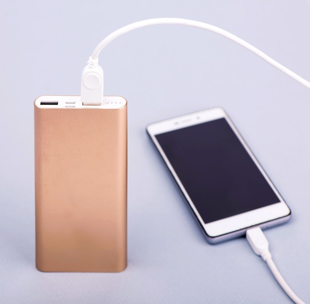 Aufladen des Smartphones mit Power Bank und Telefon auf grauer Oberfläche.