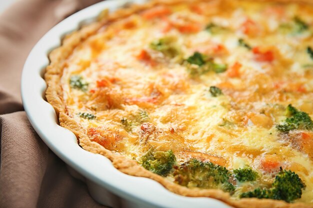 Auflaufform mit leckerer Brokkoli-Quiche auf dem Tisch in der Nähe