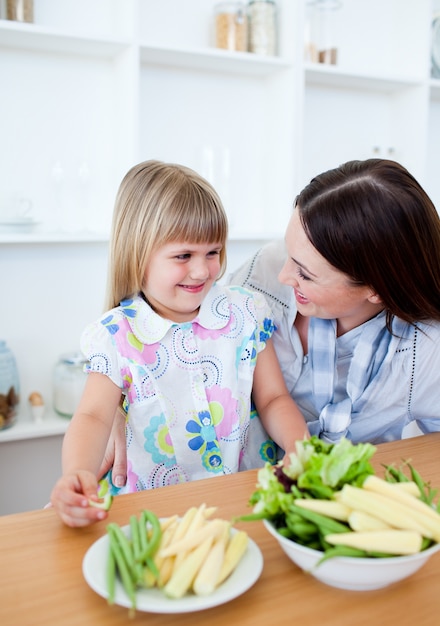 Aufmerksame Mutter und ihre Tochter, die Gemüse essen