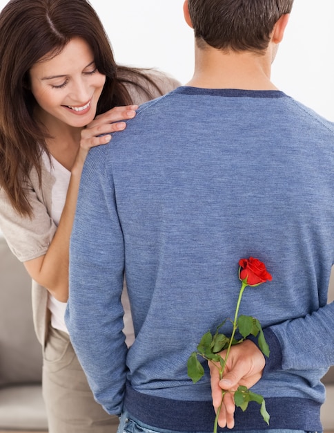 Aufmerksamer Mann, der eine Blume hinter seinem zurück für seine impatiente Freundin versteckt