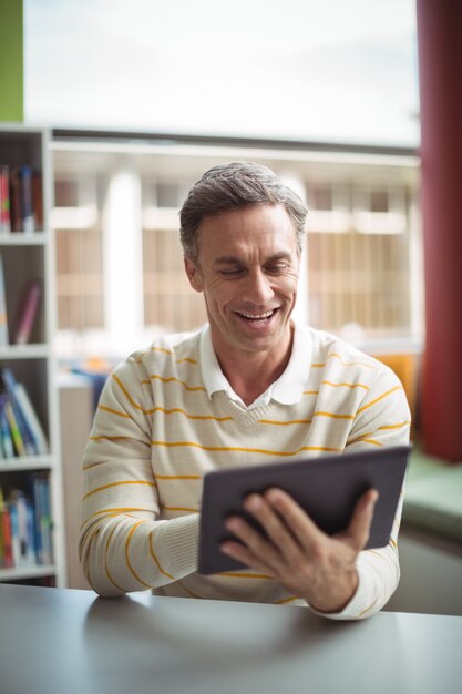 Aufmerksamer Schullehrer mit digitalem Tablet in der Bibliothek