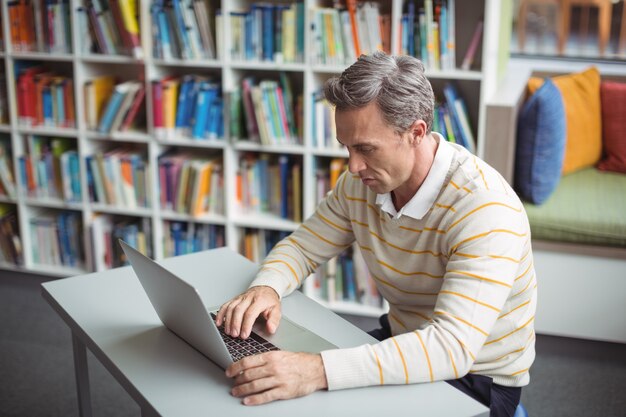 Aufmerksamer Schullehrer mit Laptop in Bibliothek