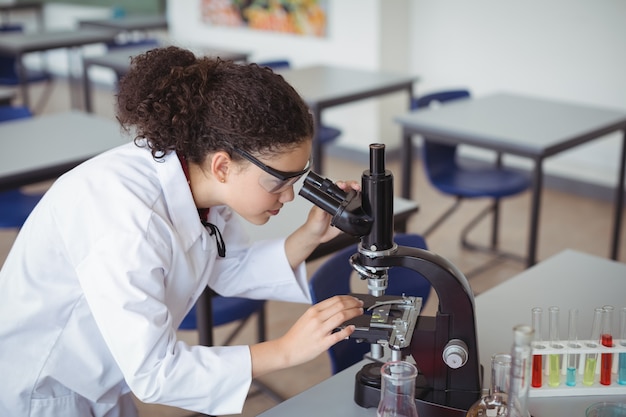 Aufmerksames Schulmädchen, das durch Mikroskop im Labor schaut