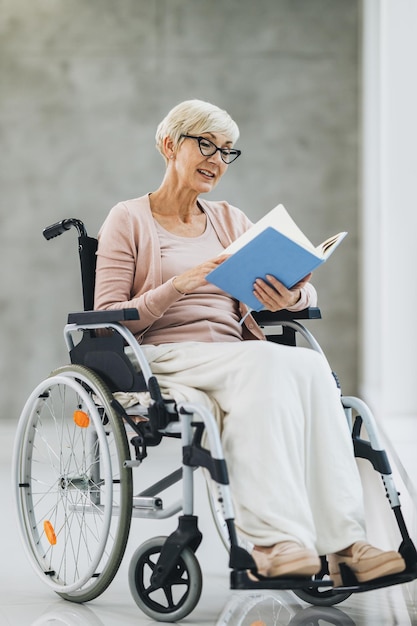 Aufnahme einer älteren Frau, die in einem Rollstuhl sitzt und ein Buch im Pflegeheim liest.