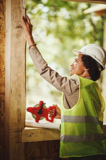 Aufnahme einer afrikanischen Architektin, die ein Fenster eines neuen Holzhauses misst.