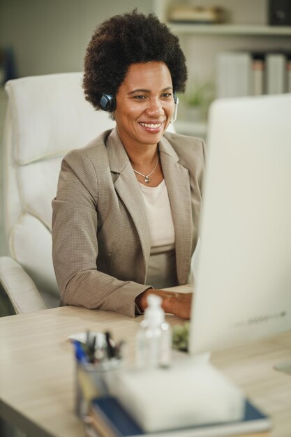 Aufnahme einer afrikanischen Geschäftsfrau, die während der COVID-19-Pandemie ein Headset trägt, während sie an ihrem Computer arbeitet.