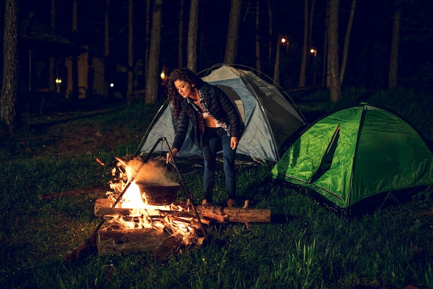 Aufnahme einer attraktiven jungen Frau, die beim Camping im Wald Abendessen kocht