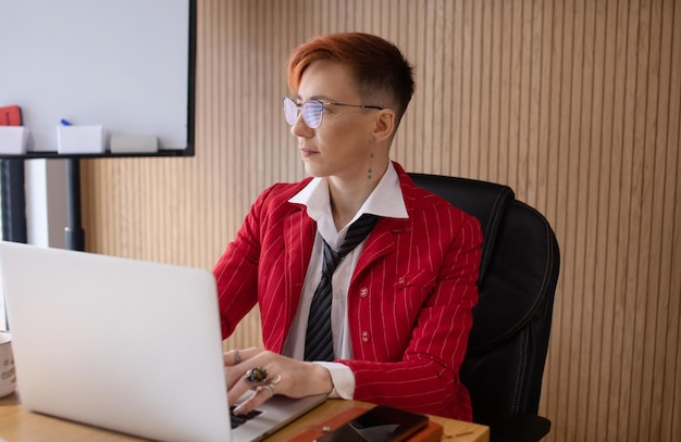Aufnahme einer attraktiven, reifen Geschäftsfrau in rotem Anzug, die an ihrem Laptop an ihrem Arbeitsplatz arbeitet