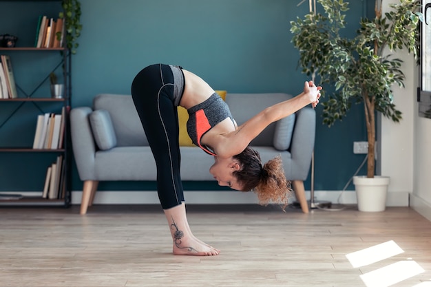 Aufnahme einer attraktiven sportlichen jungen Frau, die zu Hause hypopressive Übungen im Wohnzimmer macht.