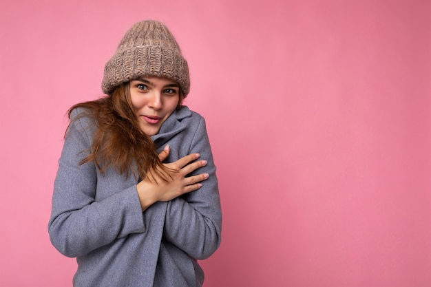 Aufnahme einer charmanten positiven jungen brünetten weiblichen Person, die über rosafarbener Hintergrundwand isoliert ist