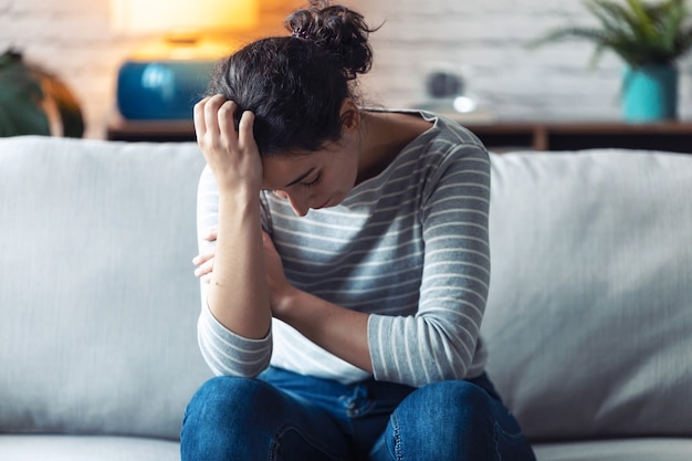 Aufnahme einer depressiven jungen Frau, die über ihre Probleme nachdenkt, während sie zu Hause auf dem Sofa sitzt.