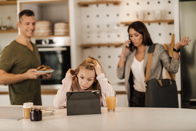 Aufnahme einer frustrierten Teenagerin, die ein digitales Tablet benutzt und darauf wartet, dass ihre gestresste Mutter mit dem Smartphone fertig ist, während sie sich auf die Arbeit vorbereitet.