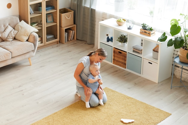 Aufnahme einer glücklichen jungen Mutter, die zu Hause Zeit mit ihrem schönen Baby auf dem Boden sitzt