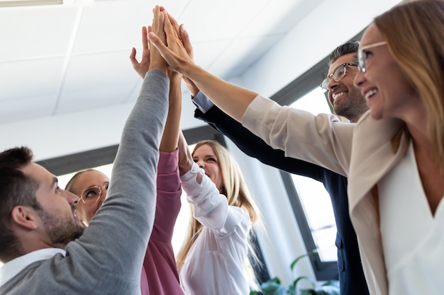 Aufnahme einer Gruppe erfolgreicher junger Geschäftsleute, die ihre rechten Hände am Coworking-Platz halten.