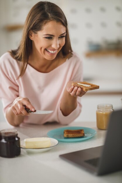 Aufnahme einer jungen Frau, die in ihrer Küche Butter auf Toast streicht.