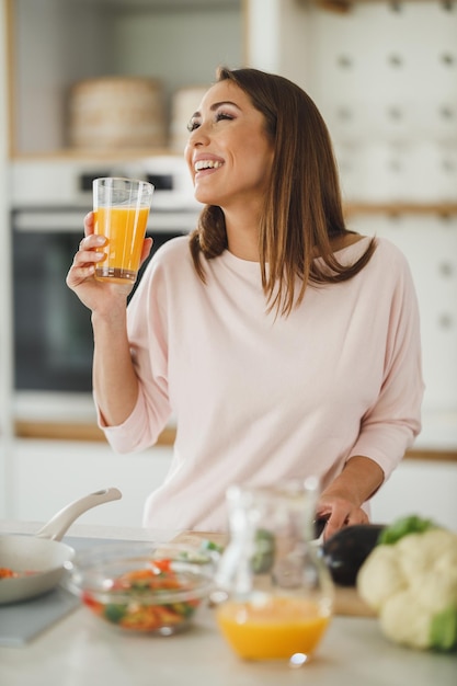 Aufnahme einer jungen Frau, die in ihrer Küche frischen Orangensaft trinkt.