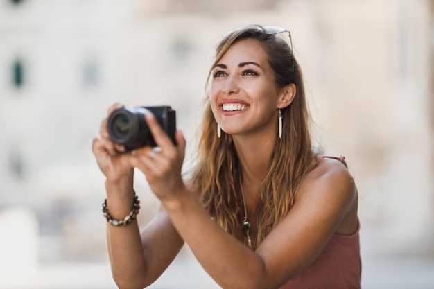 Aufnahme einer jungen lächelnden Frau, die Fotos macht, während sie eine fremde Stadt erkundet.