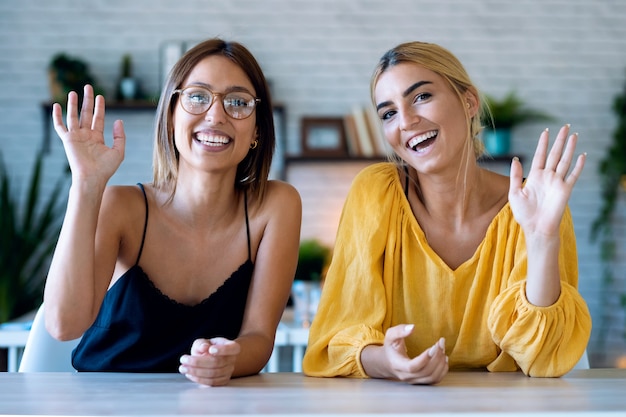 Aufnahme einer lächelnden jungen Frau, die durch die Webcam schaut und spricht, während sie eine Videokonferenz in ihrem kleinen Startup-Unternehmen macht.