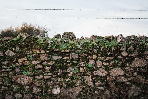 Aufnahme einer Mauer aus Steinen mit Vegetation Es hat einen Zaun darüber Es ist auf dem Land