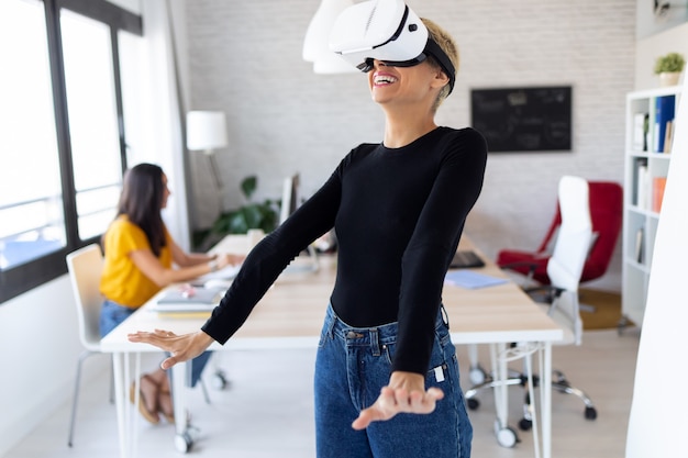 Aufnahme einer modernen jungen Unternehmerin, die ein Virtual-Reality-Headset verwendet und den Moment im Büro genießt.