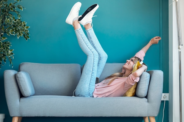 Aufnahme einer motivierten jungen Frau, die mit Smartphone Musik hört, während sie zu Hause auf dem Sofa liegt.