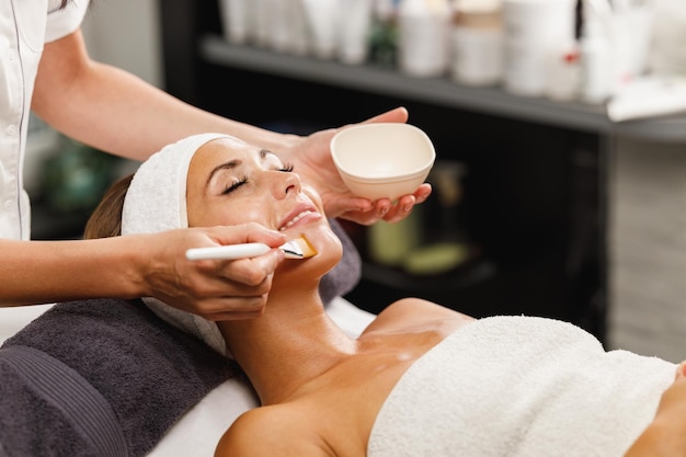 Foto aufnahme einer schönen jungen frau, die im schönheitssalon eine gesichtsmaskenbehandlung erhält.