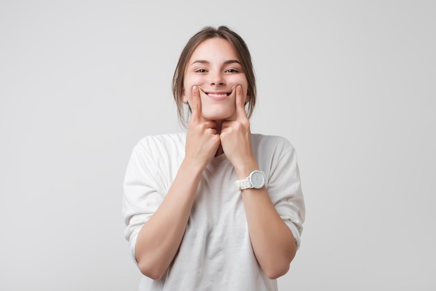 Aufnahme einer schönen kaukasischen Teenagerin, die ein Lächeln erzwingt und ihre Finger an den Rändern ihrer Lippen hält