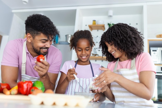 Aufnahme einer schönen, süßen Familie, die sich beim gemeinsamen Kochen in der Küche zu Hause amüsiert Süßes kleines Mädchen und ihre schönen Eltern lächeln, während sie zu Hause in der Küche kochen