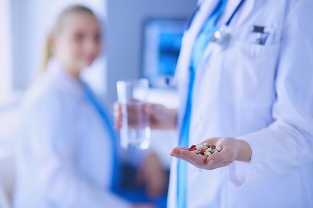 Aufnahme eines Arztes mit Pillen und einem Glas Wasser in der Klinik mit einem Kollegen im Hintergrund.