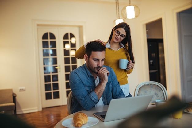 Aufnahme eines besorgten jungen Mannes, der an seinem Computer arbeitet. Seine Freundin tröstet ihn