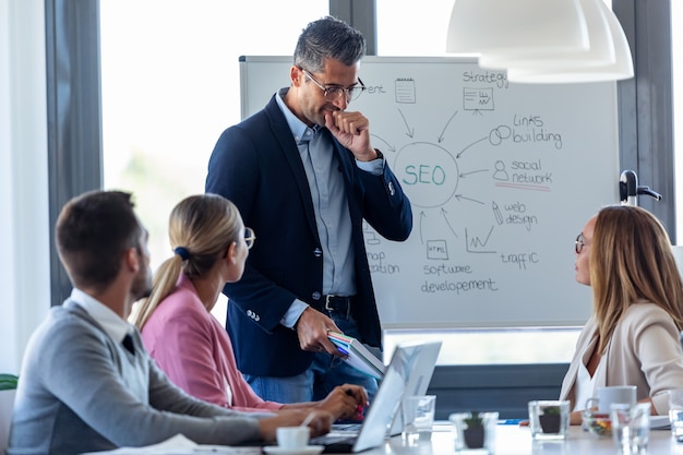 Aufnahme eines gutaussehenden Geschäftsmannes, der sich räuspert, während er seinen Kollegen am Coworking-Platz ein Projekt erklärt.