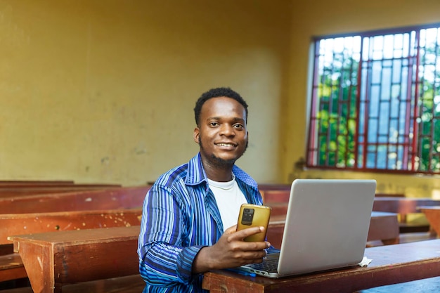 Aufnahme eines jungen gutaussehenden schwarzen afroamerikanischen Studenten, der allein im Unterricht mit dem Handy sitzt