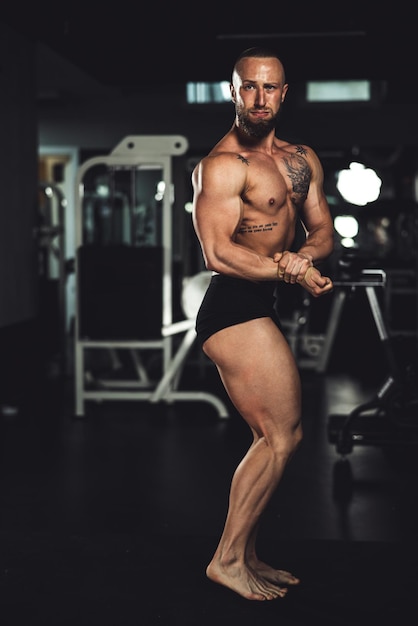 Aufnahme eines jungen muskulösen Bodybuilders, der seine perfekten Muskeln zeigt, während er nach dem Training im Fitnessstudio posiert.